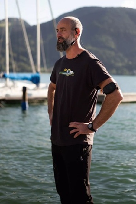Mann steht am See und beobachtet eine Situation. Am Arm trägt er ein CEECOACH PLUS und hat ein Headset auf.