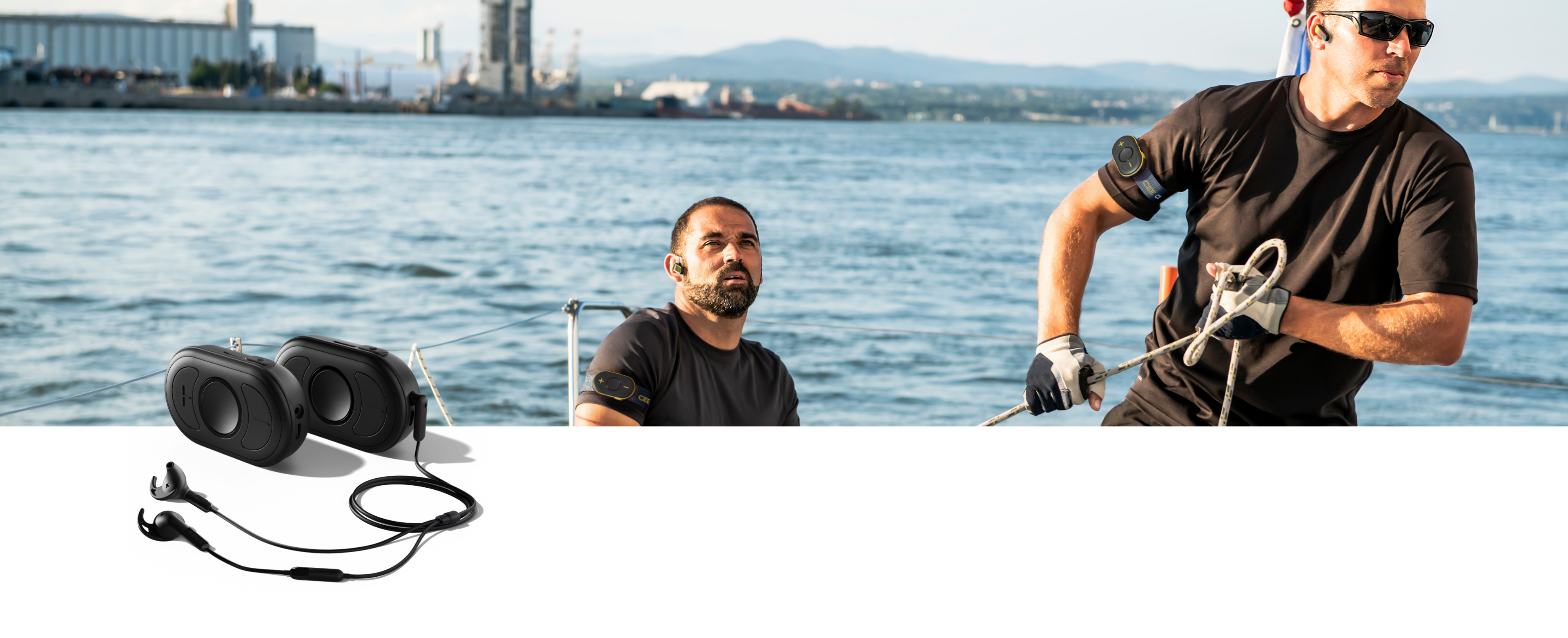 Segelboot_Zwei_Männer_Küstenlinie_im Vordergrund CEECOACH PLUS Duo_schwarz Zwei Männer an Bord eines Segelboots, einer zieht an einer Leine, der andere sitzt und schaut voraus, im Hintergrund Wasser und Küstenlinie
