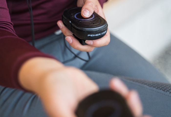 Eine Person hält zwei CEECOACH PLUS-Geräte in der Hand, wobei sie eins ihrem Gegenüber zu reichen scheint.