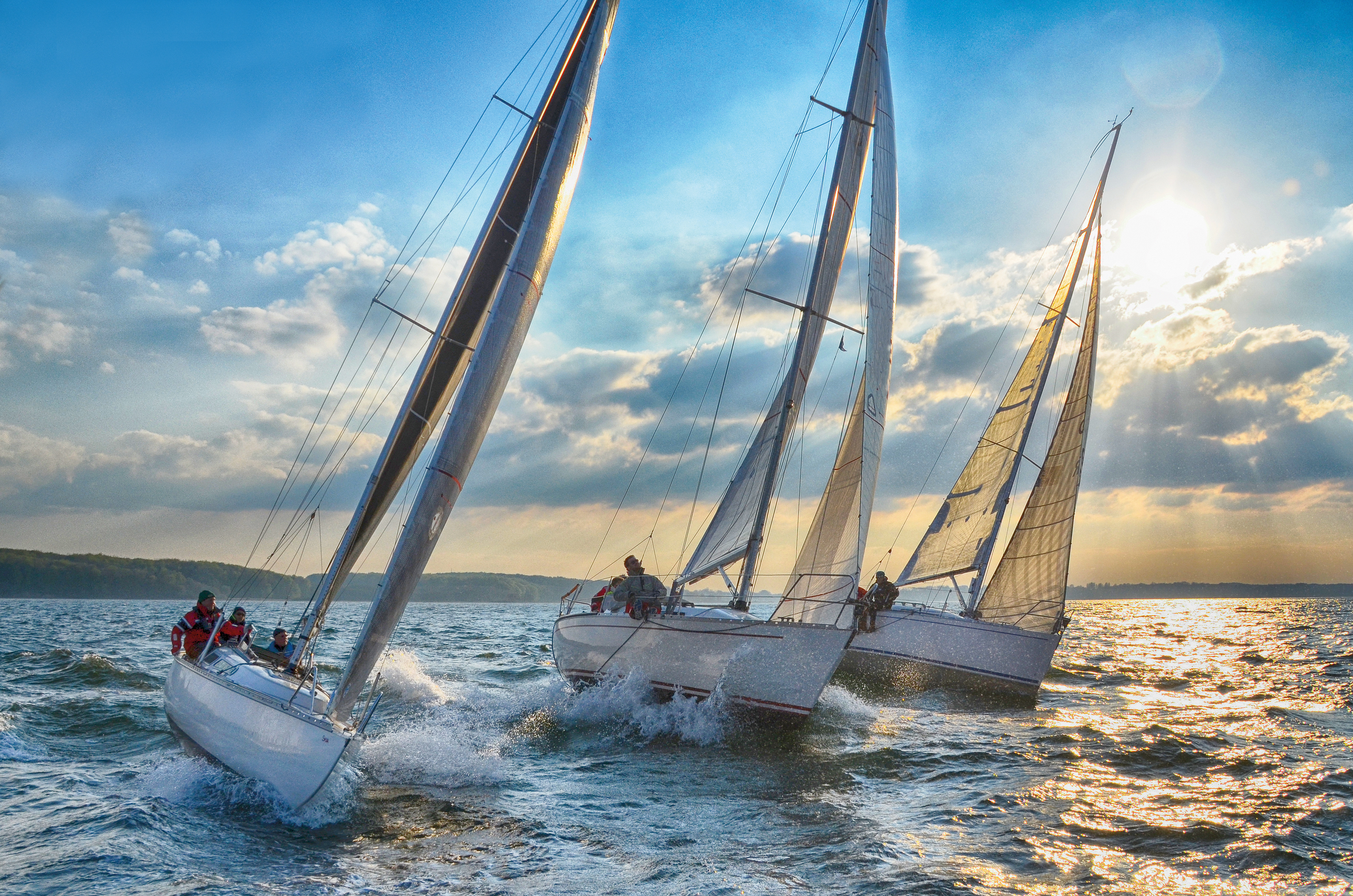 Segelboote_weiße Segel_ auf Wasser bei Sonnenuntergang Segelboote mit weißen Segeln auf bewegtem Wasser bei Sonnenuntergang