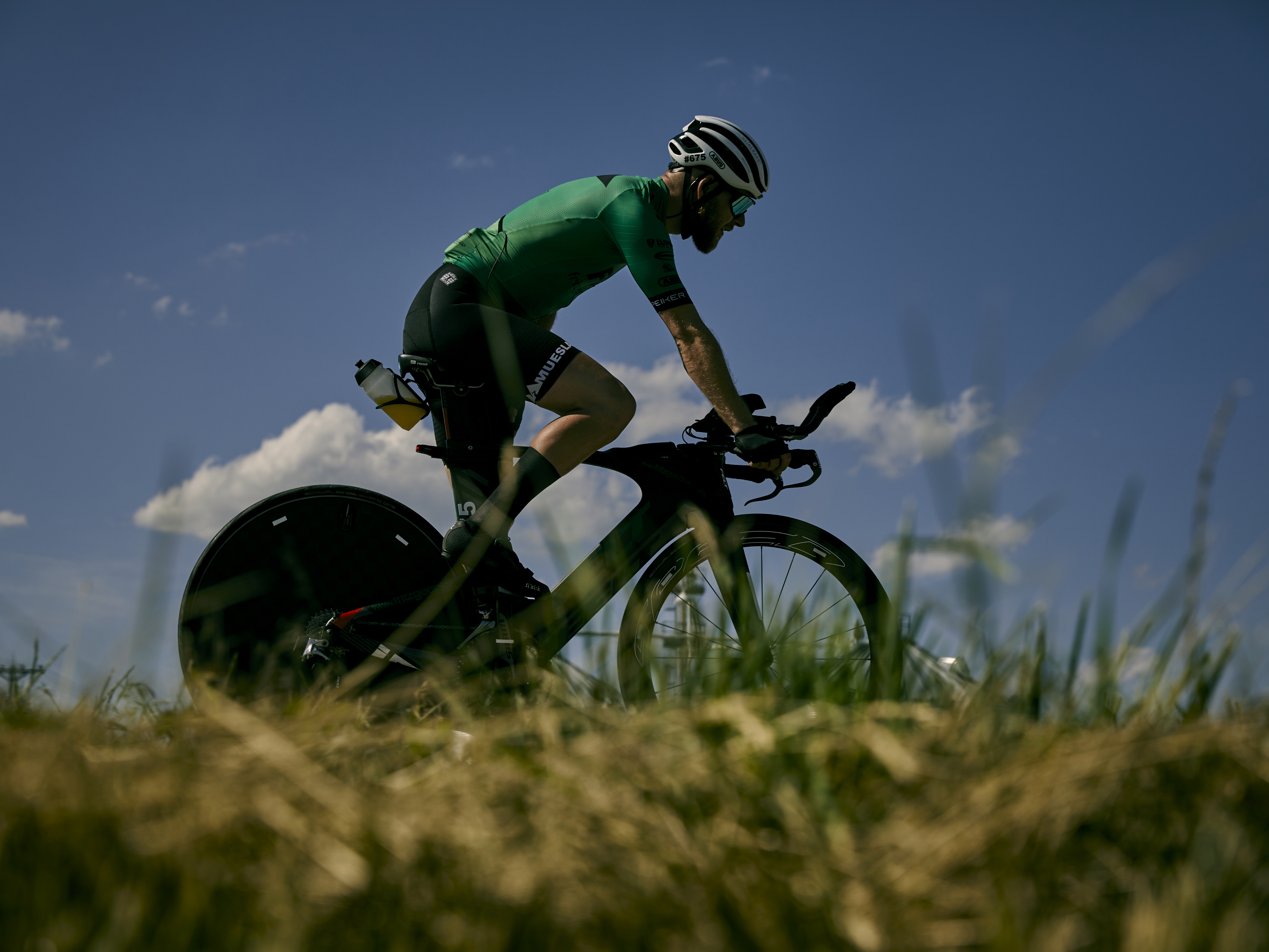 Fritz Geers auf seinem Mountainbike. Er trägt ein grünes Trikot, Fahrradhelm und Sonnenbrille. Ländliche Landschaft.