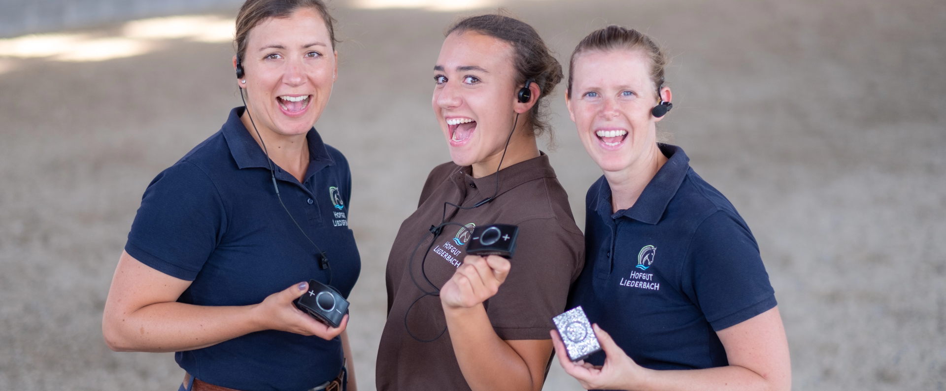 Drei lächelnde Frauen in Polo-Shirts mit Headsets und Geräten in der Hand_stehen nebeneinander_hellen Umgebung CEESSORIES_Drei lächelnde Frauen in Polo-Shirts mit Headsets und CEECOACH-Geräten in der Hand, stehen nebeneinander in einer hellen Umgebung