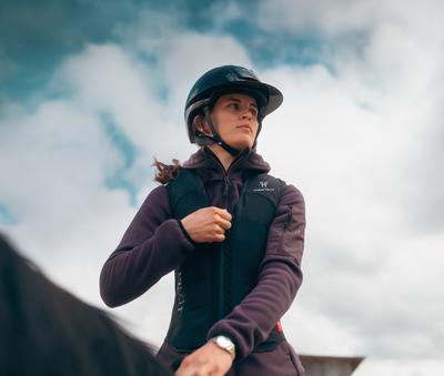 Close-up of a female rider wearing a helmet as she puts on her Horse Pilot E-Twist'Air airbag vest. Close-up of a female rider wearing a helmet on a horse, putting on her Horse Pilot E-Twist'Air airbag vest.