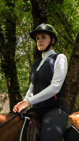 Eine Reiterin auf einem Pferd im Wald hat eine Horse Pilot E-Twist'Air Airbag-Weste an_von vorne.