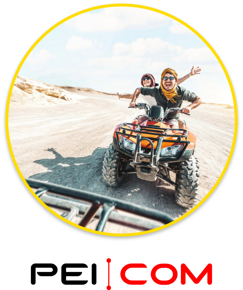 peicom_Zwei Personen fahren auf Quad_helle Wüstenlandschaft_hintere Person streckt die Arme aus Zwei Personen fahren auf einem orangefarbenen Quad durch eine helle Wüstenlandschaft, die hintere Person streckt die Arme aus