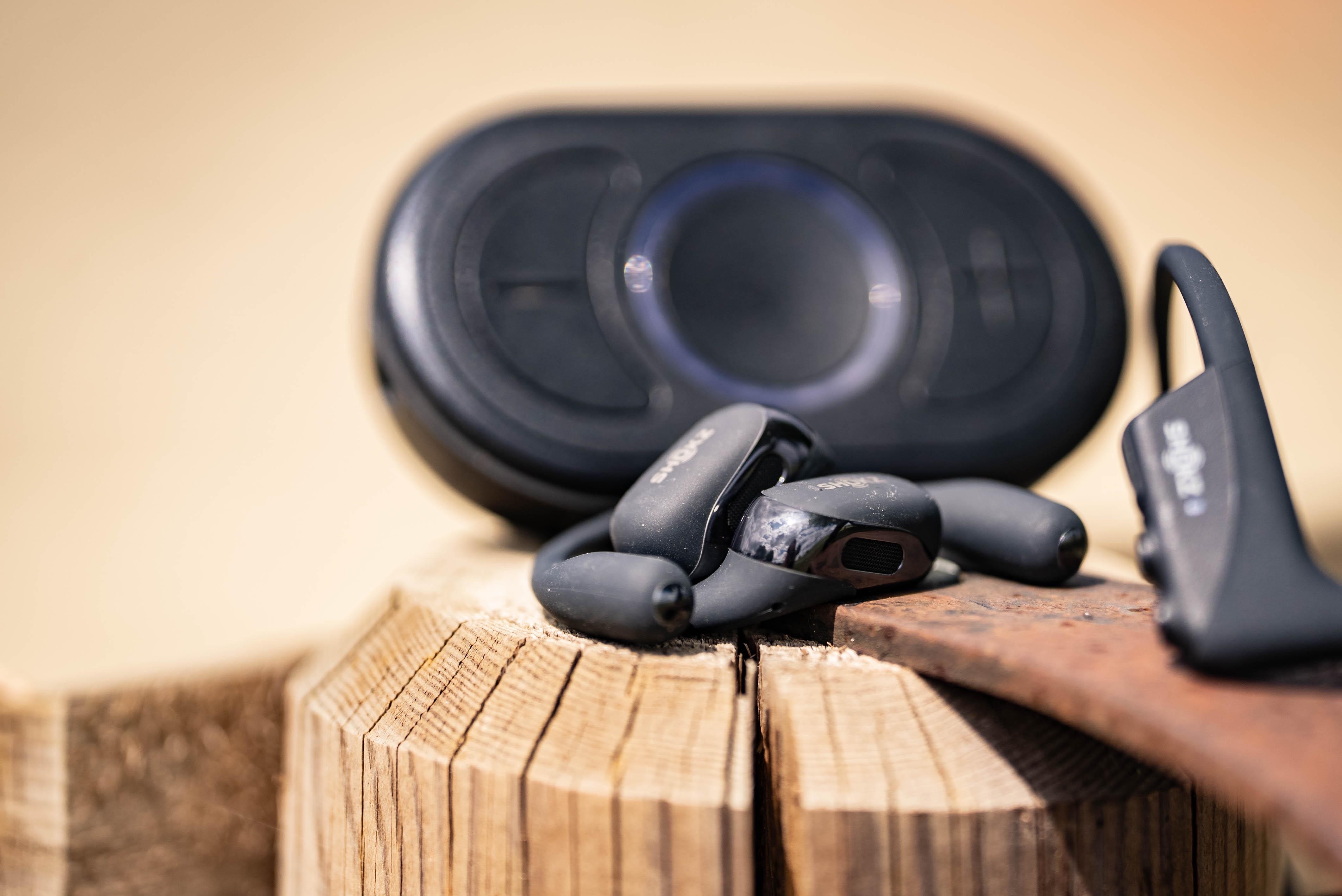 CEECOACH PLUS mit SHOKZ-Headsets liegen auf einer Holzoberfläche.  Im Vordergrund ist ein Headset scharf fokussiert, während Hintergrund und Umgebung durch eine geringe Tiefenschärfe weich verschwimmen.