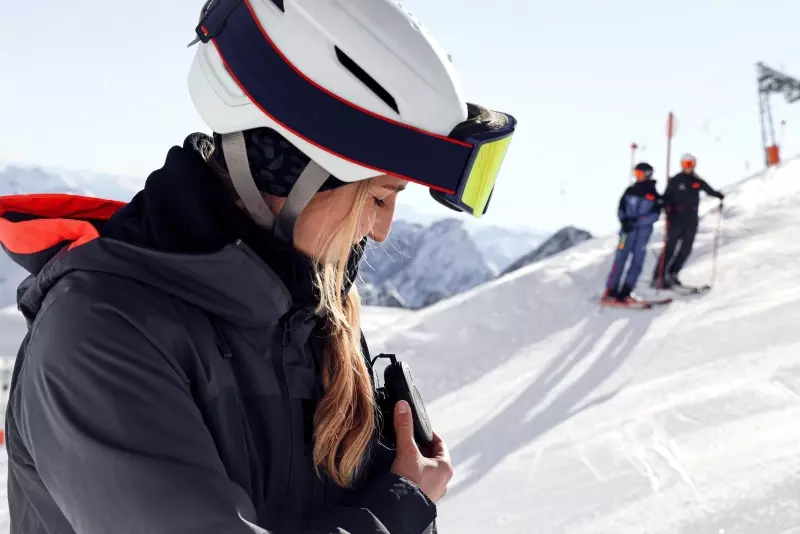 Eine Frau in Skiausrüstung_CEECOACH PLUS_Im Hintergrund ist ein Skigebiet zu sehen CEECOACH PLUS_Eine Frau in Skiausrüstung bedient ihr CEECOACH PLUS und lächelt_Im Hintergrund ist ein Skigebiet zu sehen