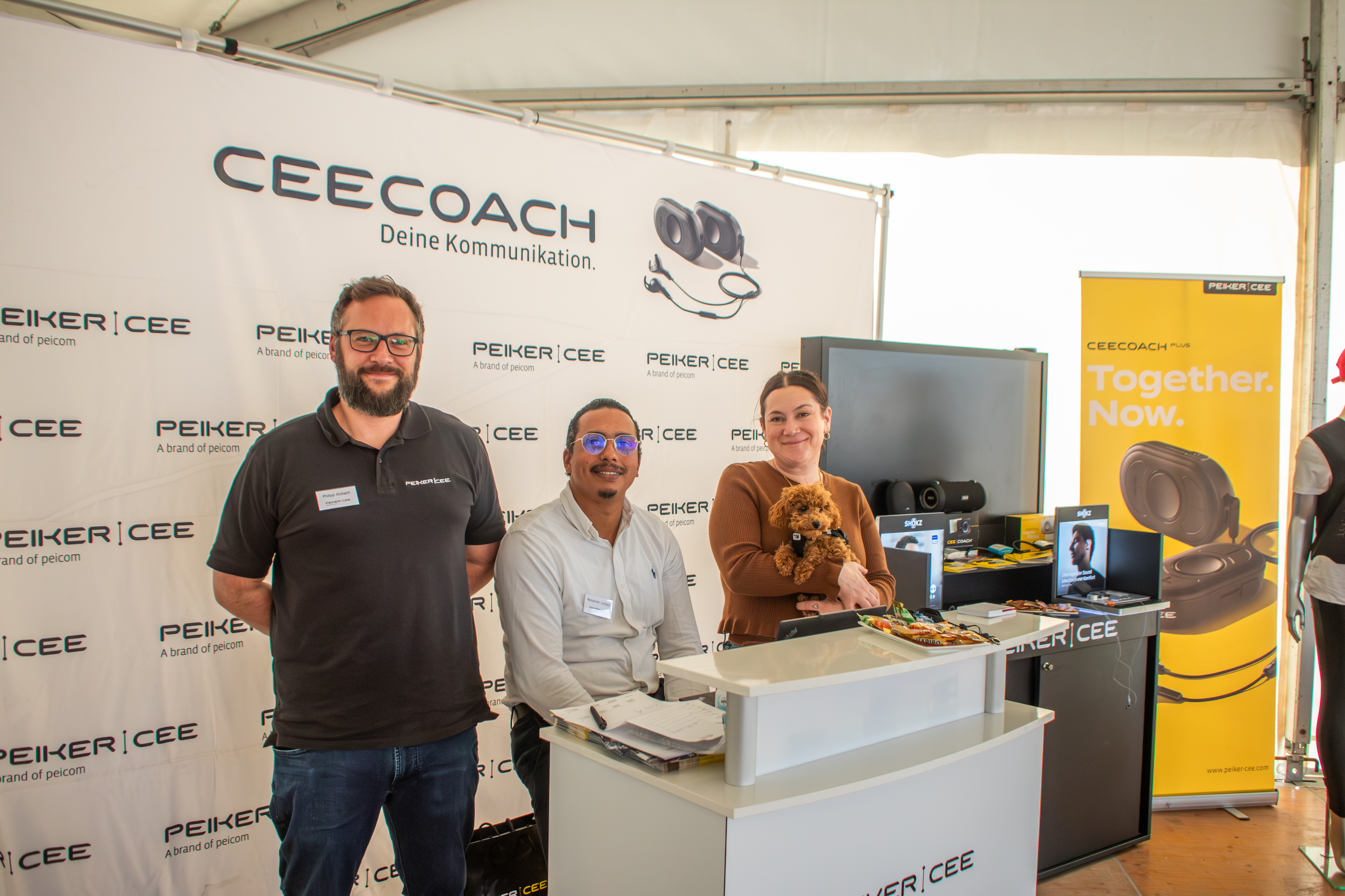 Drei Mitarbeitende stehen an einem peiker CEE Messestand auf dem Skyline Cup mit Infomaterial; im Hintergrund sind das CEECOACH-Logo, ein Produktbanner und Kommunikationsgeräte zu sehen.