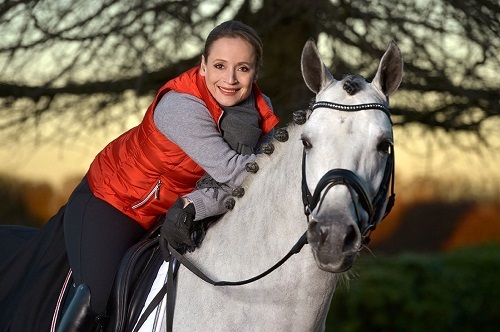 Isabell Werth sits on her horse and smiles at the camera. A sunset can be seen in the background.
